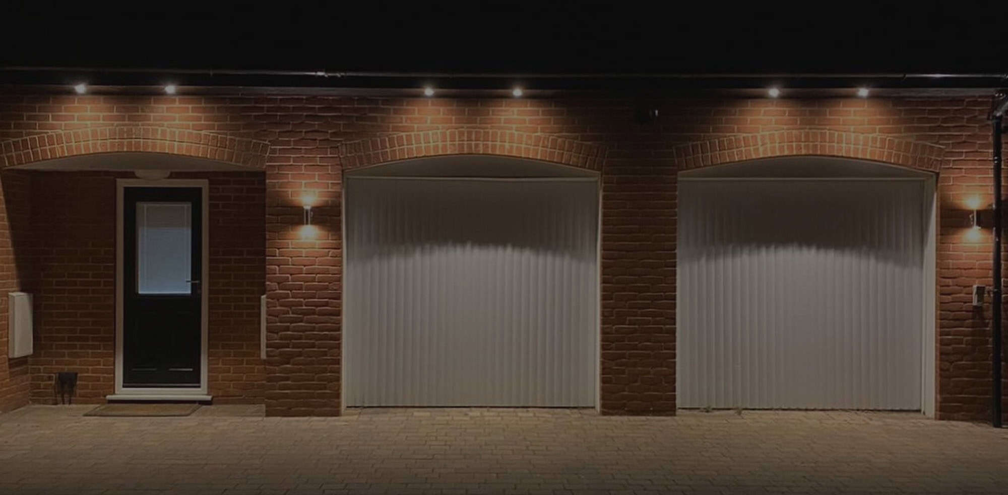 Brick garage with illuminated doors at night.