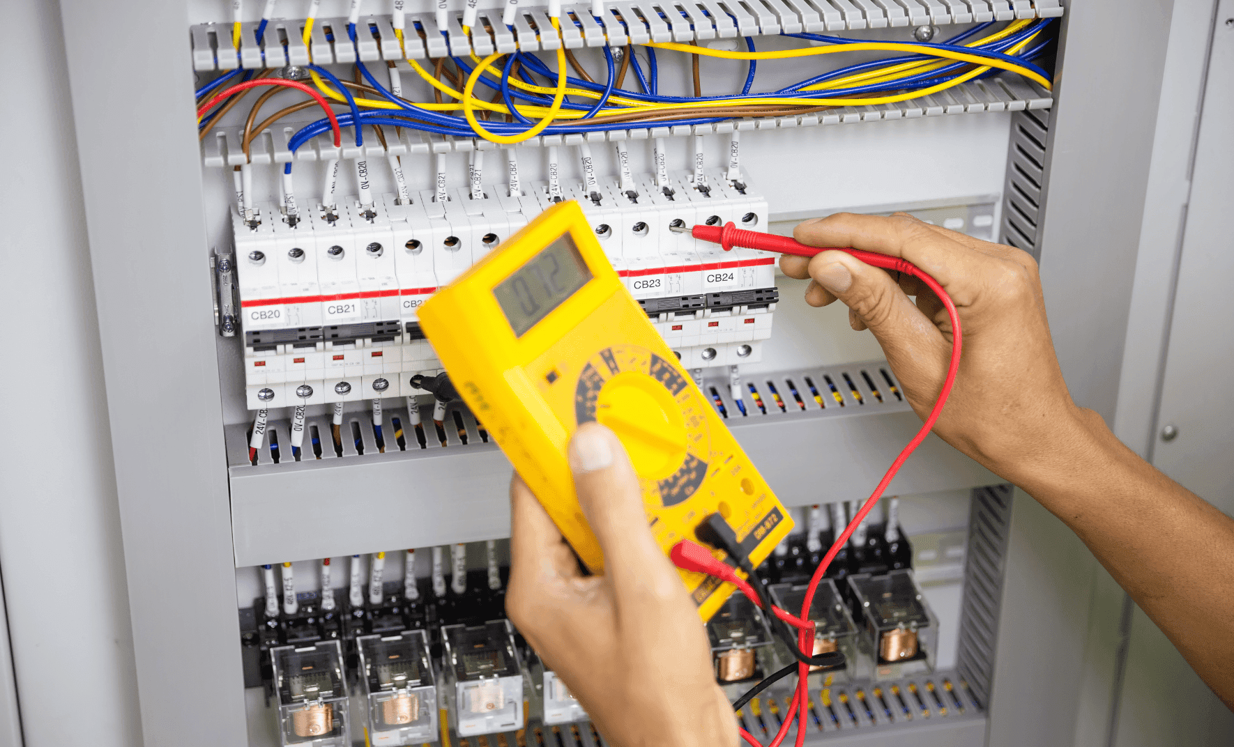 Electrician using multimeter on circuit breaker panel.