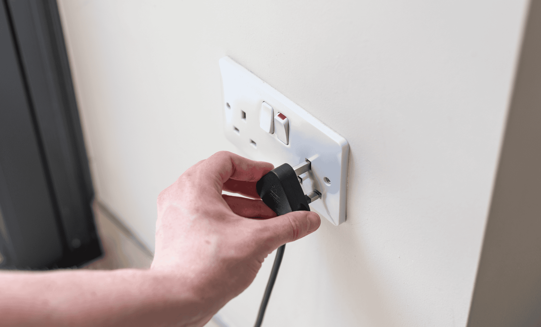 Hand plugging UK plug into wall socket